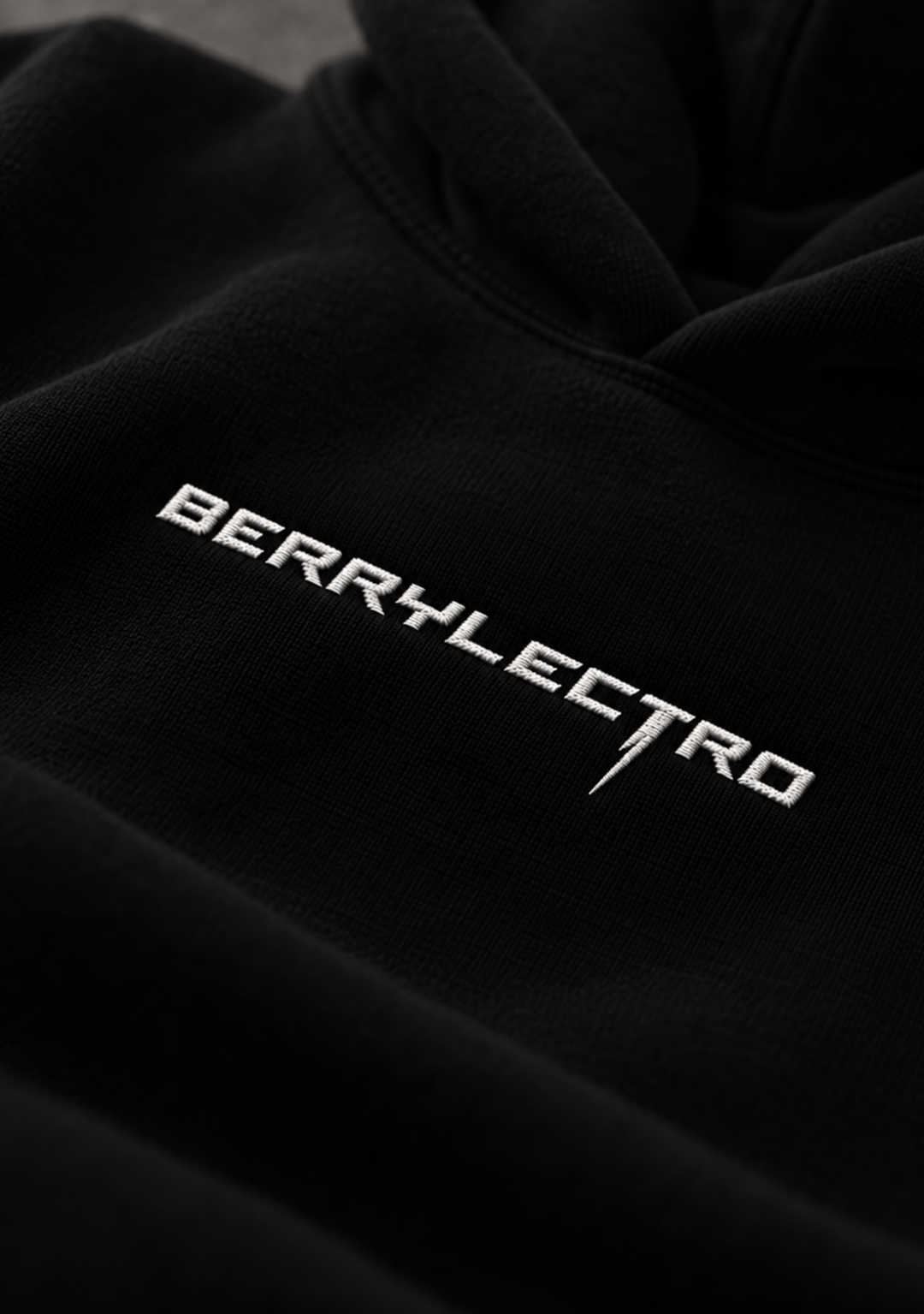 Nahaufnahme des weiß gestickten BERRYLECTRO Schriftzugs auf schwarzem Stoff, Detailansicht der Bruststickerei von Stay Lifted Collective