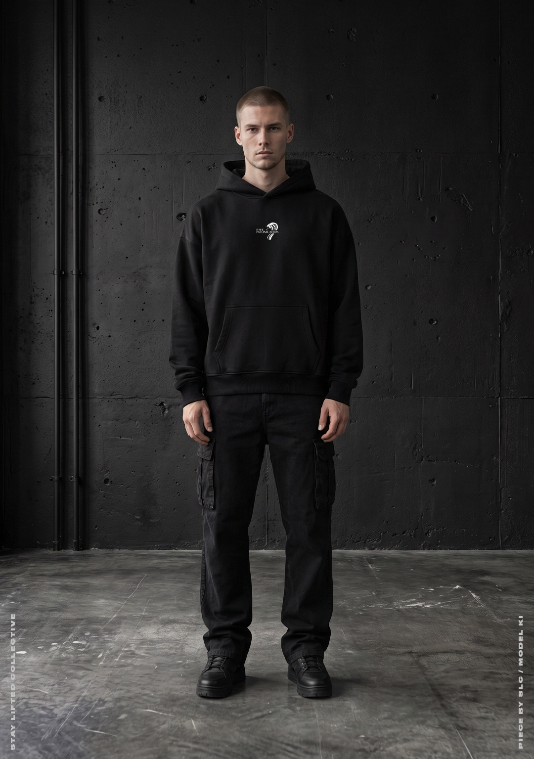 Model von vorne im schwarzen Rave Intoxication Oversized Hoodie mit kleinem weißem Rave Intoxication Logo auf der Brust und Kängurutasche vor Betonwand, Techno Streetwear von Stay Lifted Collective